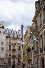Fototapeta premium Vertical view of Eiffel Tower behind traditional Parisian buildings with French flag on cloudy day