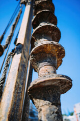Vertical view of a large industrial auger drill used in construction and earth drilling. The image captures the full length of the spiral drill bit with surrounding cables