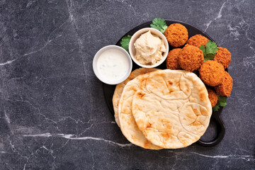 Delicious falafels and pita bread with tzatziki and hummus. Above view on a dark stone background.