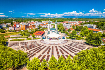 Drone image of Medjugorje showing central church, large open square, surrounding buildings and visitors gathered at this Christian pilgrimage site under clear skies in summer