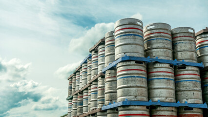 Stacked metal beer kegs under a cloudy sky