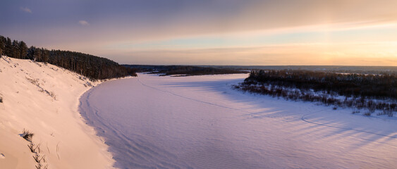 A river covered with snow illuminated by the setting sun in a winter forest.