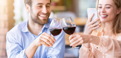Young woman making photo of romantic toast with clinking wine glasses during festive dinner at cafe, selective focus. Affectionate couple celebrating Valentine's Day or anniversary