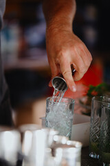 Bartender pours strong alcohol from measuring cup into a glass. Making a Mojito