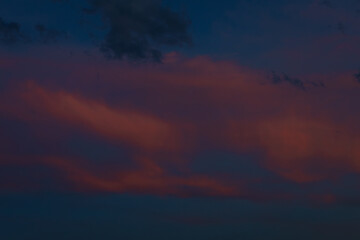 Scattered dark clouds float across a twilight sky bathed in deep blue and delicate pink tones, creating a peaceful and moody scene with copy space.