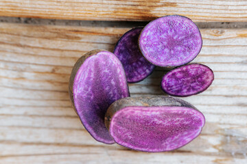 Bright cross-sections of purple potatoes displayed on rustic wooden boards, highlighting their deep color and natural marbling patterns.