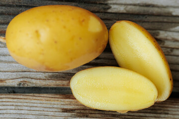 A whole yellow potato and two halves placed on a rustic wooden base, revealing a smooth, creamy interior and the natural texture of the skin.