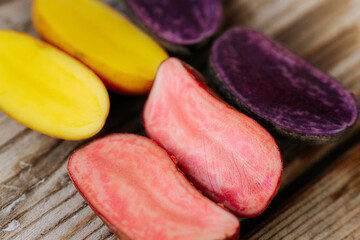 Six potato halves in bright yellow, pink and purple tones arranged on a wooden surface, showcasing their inner diversity. Space for text included.