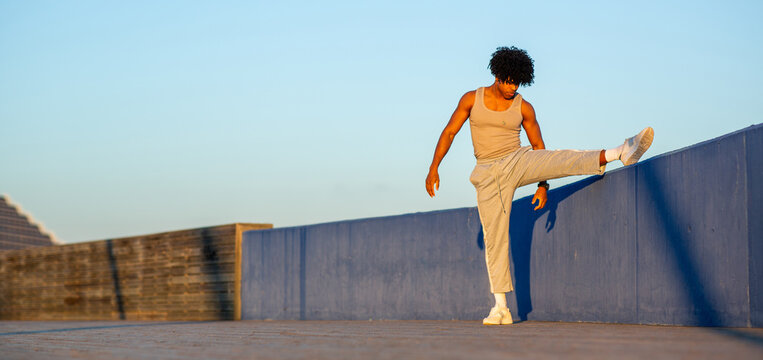 Young African American athlete stretching leg on wall in outdoor fitness routine