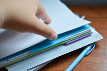close-up of a hand flipping through pages of a squared notebook with colorful covers, on a wooden desk student life, studying and revision, education materials, planning and journaling