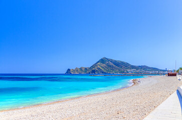Fototapeta premium Pebbe beach in Altea town on Costa Blanca coast, mountain Sierra Helada, coastline Altea bay Mediterranean Sea with azure turquoise water in sunny day, Alicante province, Valencian Community, Spain