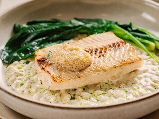 Muksun (Coregonus muksun). Muksun flesh delicacy tender. White salmon fish on pillow of pine nut garnished with blanched spinach and white caviar, on restaurant table. Delicious dish with white fish