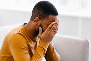 Male Depression. Desperate Depressed African Man Covering Face Crying Having Problems Sitting On Couch At Home. Emotional Stress And Unhappiness Concept. Despair, Grief And Negative Emotions