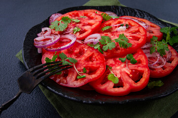 Freshly sliced tomatoes and red onions, garnished with herbs, on a black plate, summer salad, no people