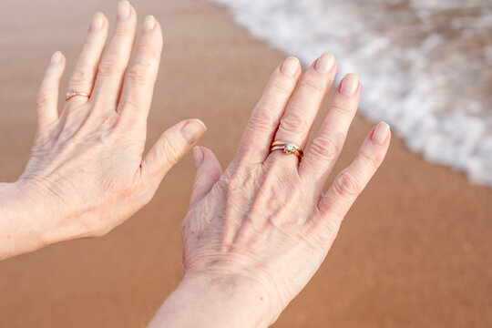 A pair of female hands with wedding rings on the background of sandy beach and sea wave