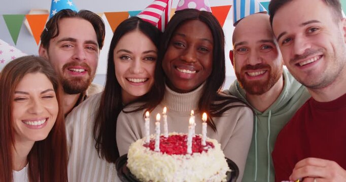 Joyful smiling multiethnic friends pose in party hats enjoy birthday party pose for making memorable photo. Happy African American woman with cake celebrates bday going to blow candles