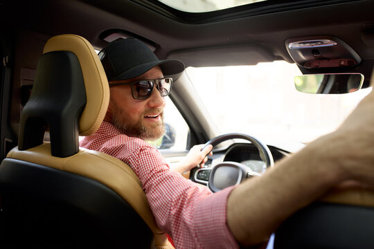 Smiling driver wearing a cap enjoying a sunny day inside a modern vehicle