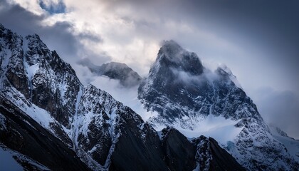 Obraz premium rugged mountain peaks rise dramatically into the sky partially hidden by swirling clouds and mist snow covers the highest elevations creating a striking contrast against the dark rock