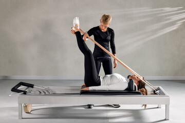 Fitness trainer assisting client with reformer Pilates exercises in a studio
