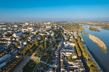 An aerial perspective captures the beauty of Saumur, France, as sunlight illuminates its architecture along the Loire River. Green landscapes and islands punctuate the flowing water