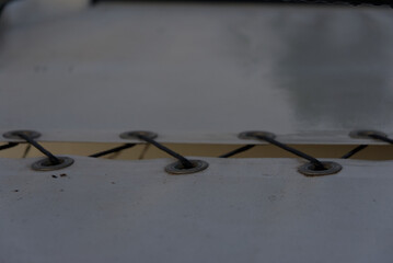 A close-up shot shows a gray tarp with silver eyelets strung together by a black cord, creating a pattern of diagonal lines against a light-colored surface.