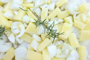 Vista cenital de patatas y cebollas troceadas con ramitas de romero fresco. Estilo minimalista y casero, ideal para recetas o fondos gastronómicos.