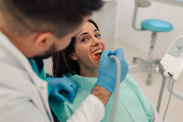 Dentist using dental equipment examining patient's teeth in clinic