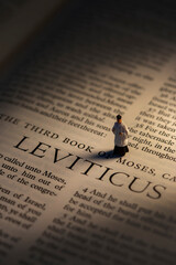 Leviticus title bible page with a backlit miniature scale model priest standing on the page. Old testament christian text concept.