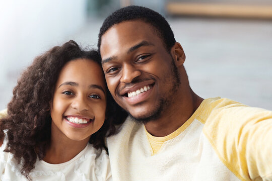 Cute african american dad and his pretty daughter taking happy selfie at home, cheerful black family having good time together, taking photos on camera or smartphone, closeup portrait