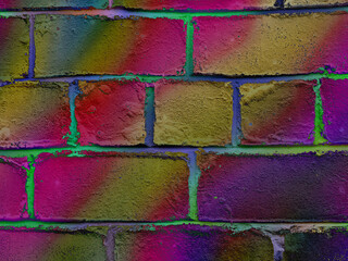 A colorful brick wall with a vibrant gradient of colors, unique texture. Close-up of a colourful bricks painted in vibrant shades of purple, pink, green and yellow shades. Bricked wall in neon colours