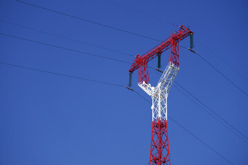 Red and white electricity pylon carrying high voltage power lines on a sunny day