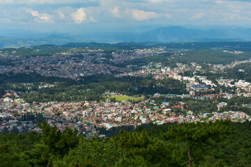 Shillong city nestled amidst hills and lush greenery, showcasing a panoramic view under a cloudy sky.