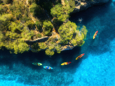 Aerial drone view of colorful kayaks, rocky coastline with pine trees and crystal clear turquoise water. Summer adventure in Mallorca, Balearic Islands, Spain. Mediterranean sea. Top view of canoes