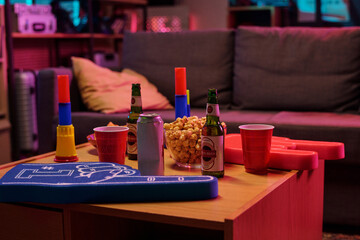 Table holding popcorn, beer bottles, soda can, plastic cups, foam fingers and colorful noisemakers in living room setting, suggesting preparation for sports viewing or party gathering