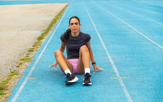 Young woman athlete sitting on blue running track recovering after a calf injury - Powered by Adobe