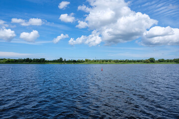 A tranquil lake scene with blue skies and fluffy clouds, surrounded by lush green landscape - Rostock, Germany