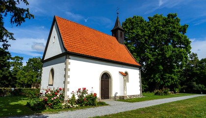 Fototapeta premium Small white chapel with a terracotta roof, surrounded by greenery and a paved path