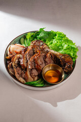 Traditional Korean dish with sliced roasted pork leg, fresh lettuce, kimchi, sesame seeds, and soy sauce. Tasty Asian cuisine captured in natural daylight.