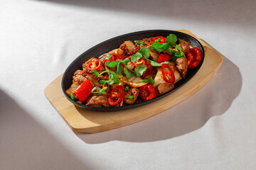 Spicy Korean stir-fry dish with juicy meat, red chili peppers, kimchi, and fresh herbs served on a hot skillet. Authentic Asian cuisine in natural light.