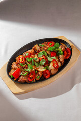 Spicy Korean stir-fry dish with juicy meat, red chili peppers, kimchi, and fresh herbs served on a hot skillet. Authentic Asian cuisine in natural light.