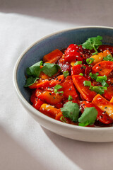 Korean rice cakes cooked in spicy gochujang sauce with vegetables, sesame seeds and fresh herbs served in ceramic bowl under natural daylight