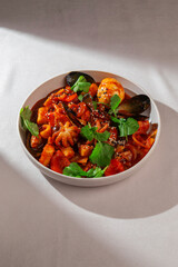 Traditional Korean tteokbokki with seafood mix including mussels, baby octopus, spicy sauce, boiled egg and sesame served in a ceramic bowl under natural daylight