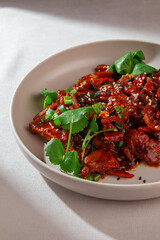 Stir-fried shrimp in Korean spicy gochujang sauce with sesame seeds, onion and fresh greens served on a ceramic plate under natural light