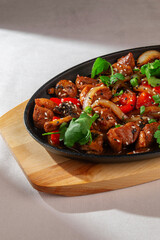 Stir-fried Korean meat with onion, bell pepper, mushrooms, sesame seeds and herbs served in a hot black skillet on wooden tray under natural light