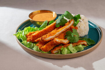 Breaded chicken katsu slices served with steamed rice topped with sesame seeds, spicy dipping sauce and fresh cilantro on a blue ceramic plate