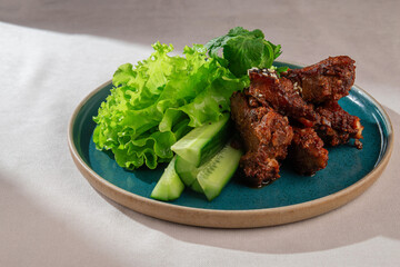 Appetizing and juicy glazed pork ribs, sprinkled with sesame seeds, served alongside crisp green lettuce and refreshing cucumber slices on a dark plate