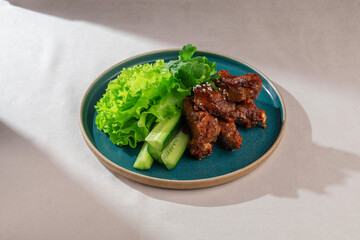 Appetizing and juicy glazed pork ribs, sprinkled with sesame seeds, served alongside crisp green lettuce and refreshing cucumber slices on a dark plate