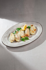 Appetizing baked mussels in their shells, topped with melted creamy cheese, garnished with fresh herbs and a bright lemon wedge, served on an oval plate