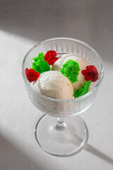 Three creamy scoops of vanilla ice cream beautifully presented in a classic glass dessert bowl, adorned with vibrant red roses and green decorative elements