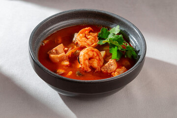 A vibrant and flavorful bowl of spicy Thai Tom Yum soup, generously filled with succulent shrimps and fresh green cilantro, perfect for a warming meal